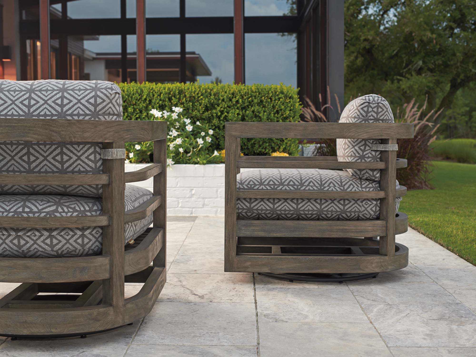 Outdoor swivel chairs with patterned performance cushions and woven wood frames on a modern patio.